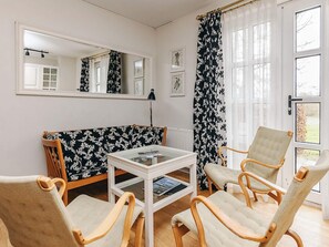 Une pièce avec un mur recouvert de miroirs, un canapé à motifs floraux, une table avec un plateau en verre et deux chaises en bois.