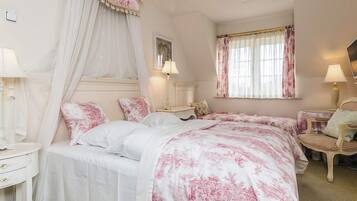 A bedroom with a canopy bed, two bedside tables, a chair, and a window with curtains.