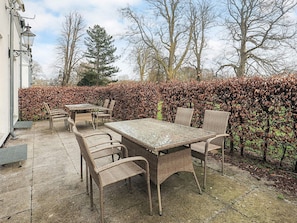 An outdoor patio with a table and chairs, a hedge, and trees in the background. - 4 Star Holiday Home in Faaborg (Faaborg)