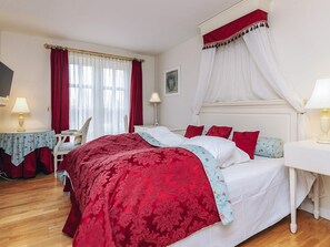 Une chambre à coucher avec un lit, une table de chevet, une chaise, une fenêtre avec des rideaux et une lampe.