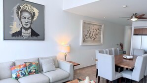 Una sala de estar moderna con sofá, una mesa de centro, una mesa de comedor, sillas, obras de arte y un ventilador de techo.