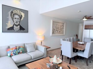 Ein modernes Wohnzimmer mit Sofa, Couchtisch, Esstisch, Stühlen, Kunstwerken und einem Deckenventilator.