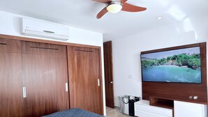 Quarto com cama, guarda-roupa, ventoinha no teto, ar condicionado, televisão e um pequeno armário.
