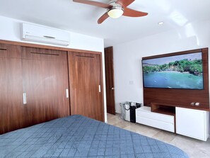 Ein Schlafzimmer mit Bett, Kleiderschrank, Deckenventilator, Klimaanlage, Fernseher und einem kleinen Schrank.