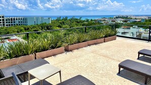 Terraço no terraço com área de estar externa, vista para o oceano e vegetação ao redor.