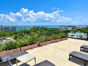 Eine Dachterrasse mit Sitzgelegenheiten im Freien, Blick auf den Ozean und umliegendes Grün.