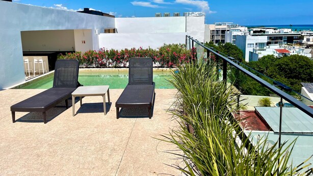 Um terraço no telhado com duas cadeiras de descanso, uma mesa pequena e uma piscina.