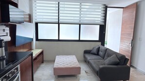 Uma sala de estar moderna com sofá, pufê, cozinha e janelas amplas.