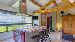 A modern kitchen with a large island, a dining area with chairs, a wooden ceiling, and a view of the countryside. - Le Clos des Vignes - VERZE (VERZE)