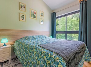 A bedroom with a bed, a nightstand, a lamp, a window with curtains, and wall art. - Le Clos des Vignes - VERZE (VERZE)