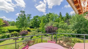 A balcony with a pink table and chairs, overlooking a lush garden with various plants and trees. - Le Clos des Vignes - VERZE (VERZE)