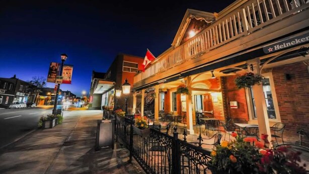 A restaurant with outdoor seating, a Heineken sign, and a red flag on the roof. - Charming Streetsville 2BR Suite-Parking & Laundry (Mississauga)