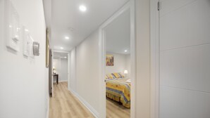 A hallway with a wooden floor leading to a bedroom with a bed and a painting on the wall. - Charming Streetsville 2BR Suite-Parking & Laundry (Mississauga)