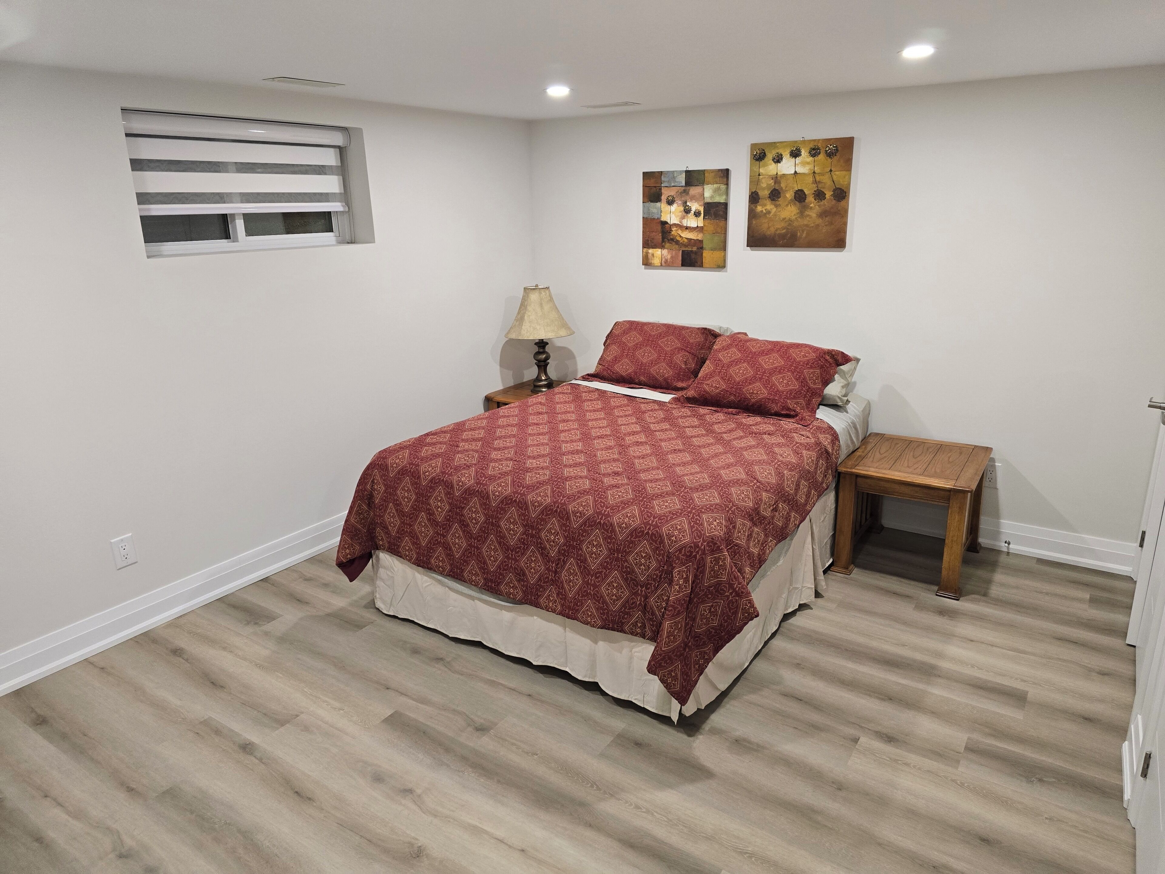 Un dormitorio con cama, mesita de noche, lámpara y dos cuadros en la pared.