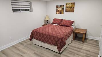 Un dormitorio con cama, mesita de noche, lámpara y dos cuadros en la pared.