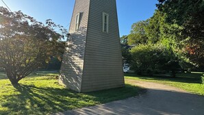 Una torre aislada con techo plano y una ventana pequeña, rodeada de hierba y árboles.