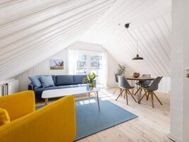 Una habitación moderna estilo loft con techo alto, un sofá azul, un sillón amarillo, una mesa de comedor con sillas y vistas al exterior.