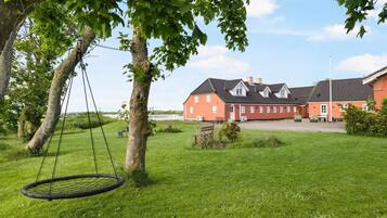 A red building with a white fence, a swing, and a grassy field.