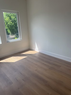Ein Zimmer mit Holzboden, einem großen Fenster und weißen Wänden.