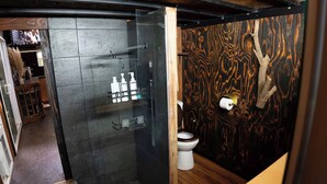 Une salle de bain moderne avec une douche à l’italienne en verre, des toilettes et un mur en bois décoré d’une branche d’arbre.