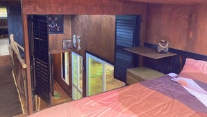 Un intérieur en bois comprenant un lit, une petite table et une fenêtre donnant sur un jardin.