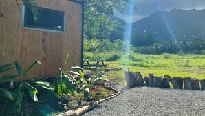 Une cabane en bois, avec un chemin de gravier menant à une table de pique-nique, entourée de verdure et avec des montagnes en arrière-plan.