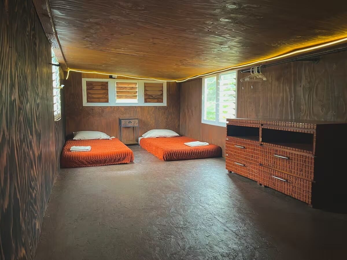A room with two beds, wooden walls, a brick cabinet, and a window.