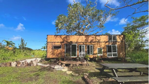Une maison en bois à l’allure rustique, dotée d’une véranda, d’un petit jardin et d’une table de pique-nique.