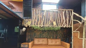 Une pièce comprenant un canapé, une petite table, une plante suspendue et un mur en bois orné de branches.