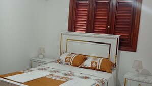 A bedroom with a bed, nightstands, a window with wooden shutters, and an air conditioning unit. - Exclusive villa for rent in Juan Dolio private second line beach 1 min. (Playa Juan Dolio)