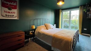 A bedroom with a bed, bedside lamp, dresser, and a framed picture of Campbell's Tomato Soup.