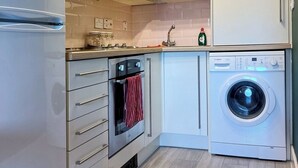 A compact kitchen with a built-in oven, a washing machine, and a stainless steel refrigerator.