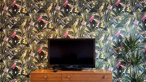 A television on a wooden cabinet against a wall with a tropical wallpaper.
