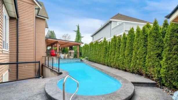 A backyard with a swimming pool, a covered patio, and a hedge. - 3BR Suite near White Rock Beach • Pool & BBQ (Surrey)