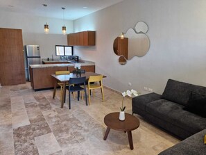 Ein modernes Wohnzimmer mit einer Couch, einem Esstisch mit Stühlen, einem kleinen Couchtisch und einer Küchenzeile inklusive Kühlschrank, Herd und Mikrowelle.