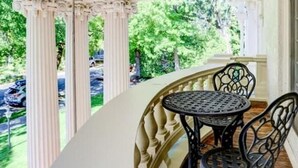 Un porche cubierto con una mesa redonda y sillas, columnas y vistas a un paisaje verde.