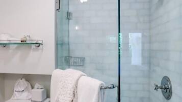 Un baño moderno con cabina de ducha de vidrio, inodoro y repisa de vidrio con artículos de aseo.