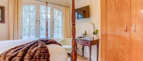 A bedroom with a four-poster bed, a wooden wardrobe, a desk with a vase, and a chair.