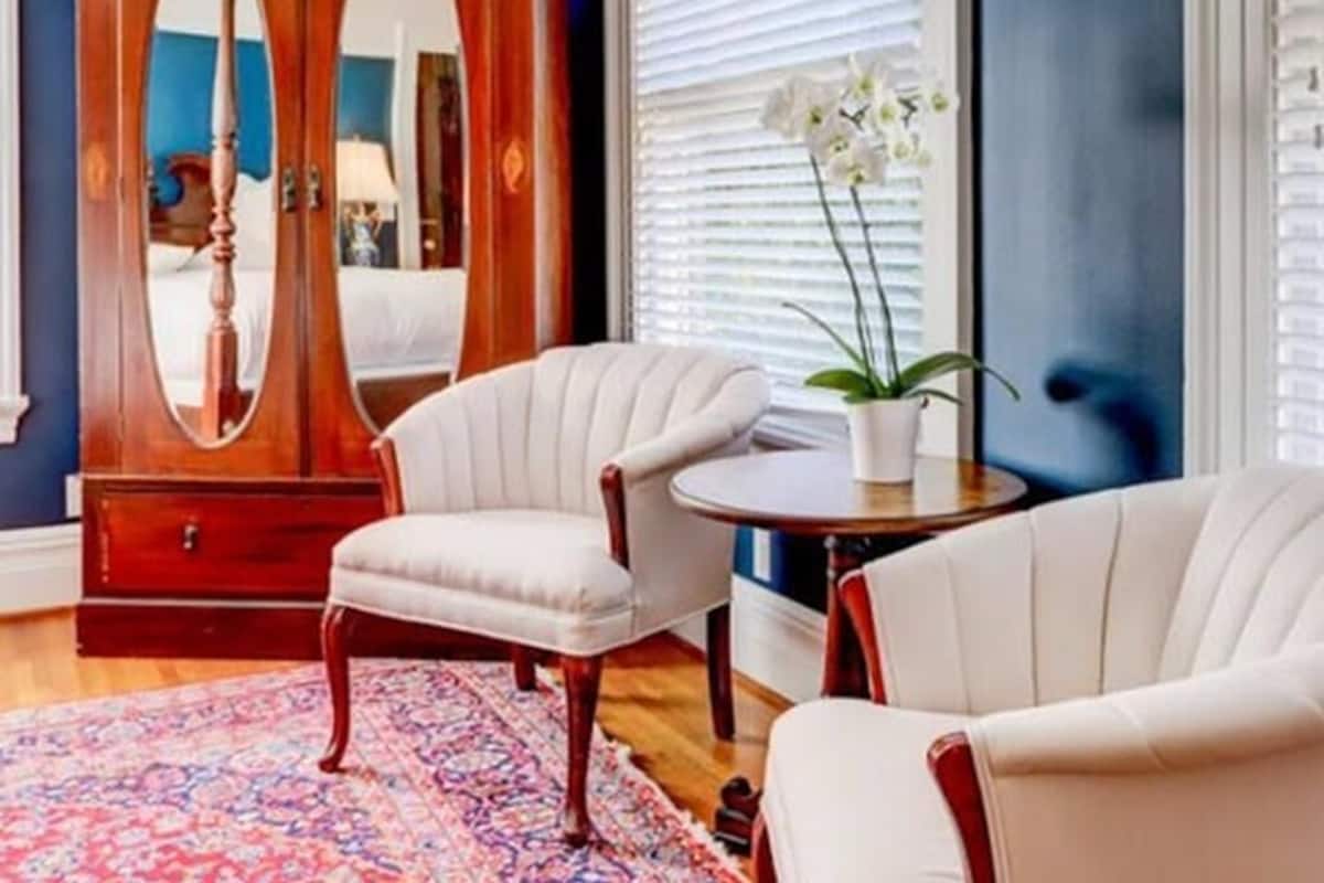 Une pièce comprenant une grande armoire en bois, deux fauteuils blancs à revêtement, une petite table ronde et un tapis à motifs.