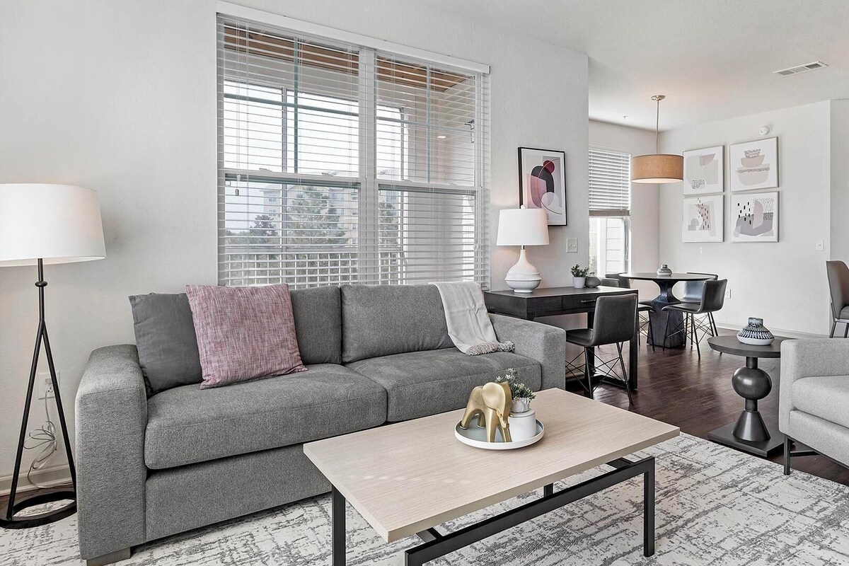 Ein modernes Wohnzimmer mit grauem Sofa, einem Couchtisch und einem Essbereich mit Tisch und Stühlen.