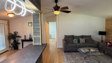 Ein modernes Wohnzimmer mit grauem Sofa, Couchtisch und Deckenventilator.