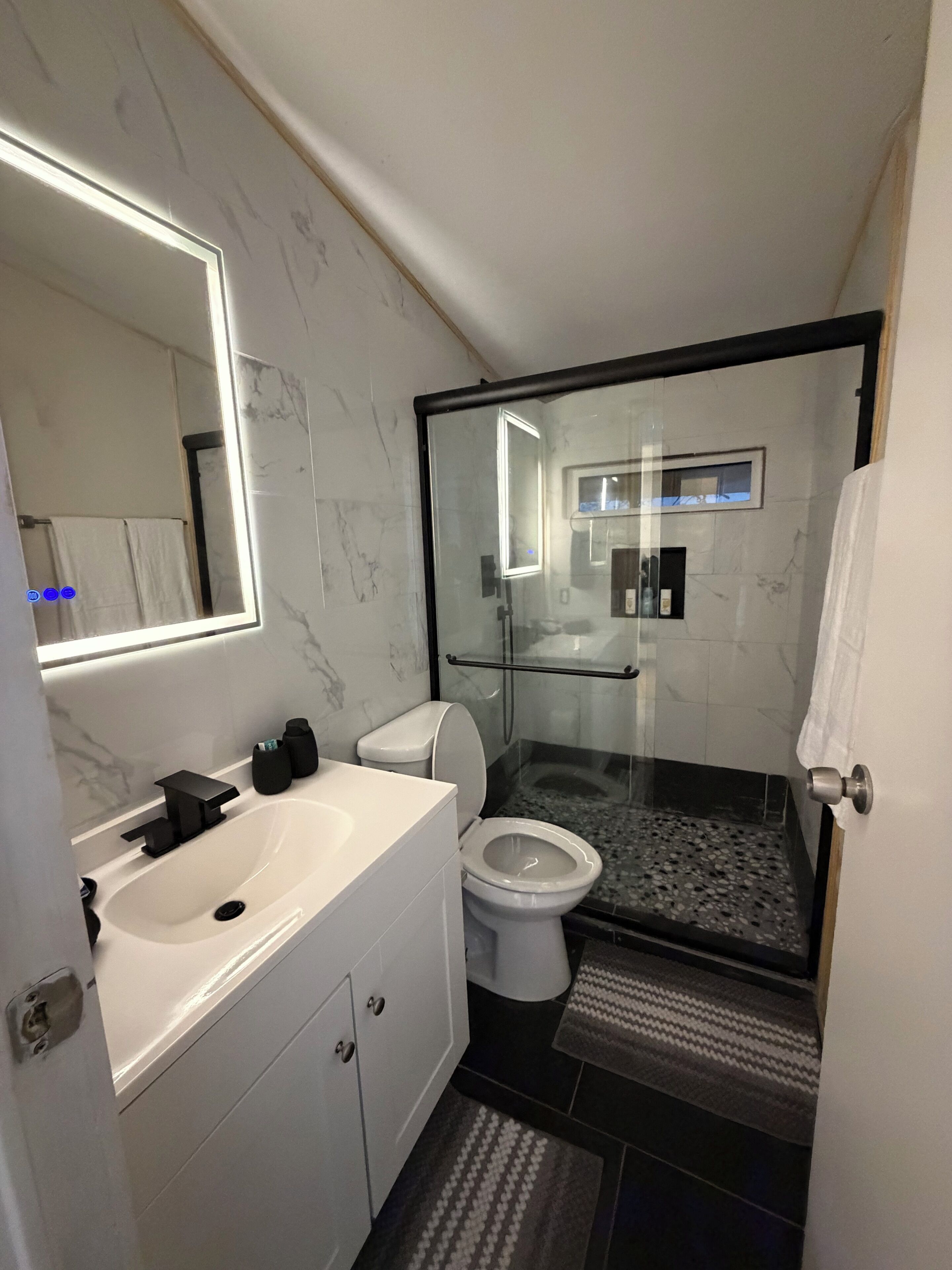 Une salle de bain moderne avec une douche à parois de verre, des toilettes blanches, un meuble-lavabo avec un miroir et un évier.