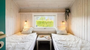 Una cabaña con dos camas, una mesita y una ventana con vista a la vegetación.