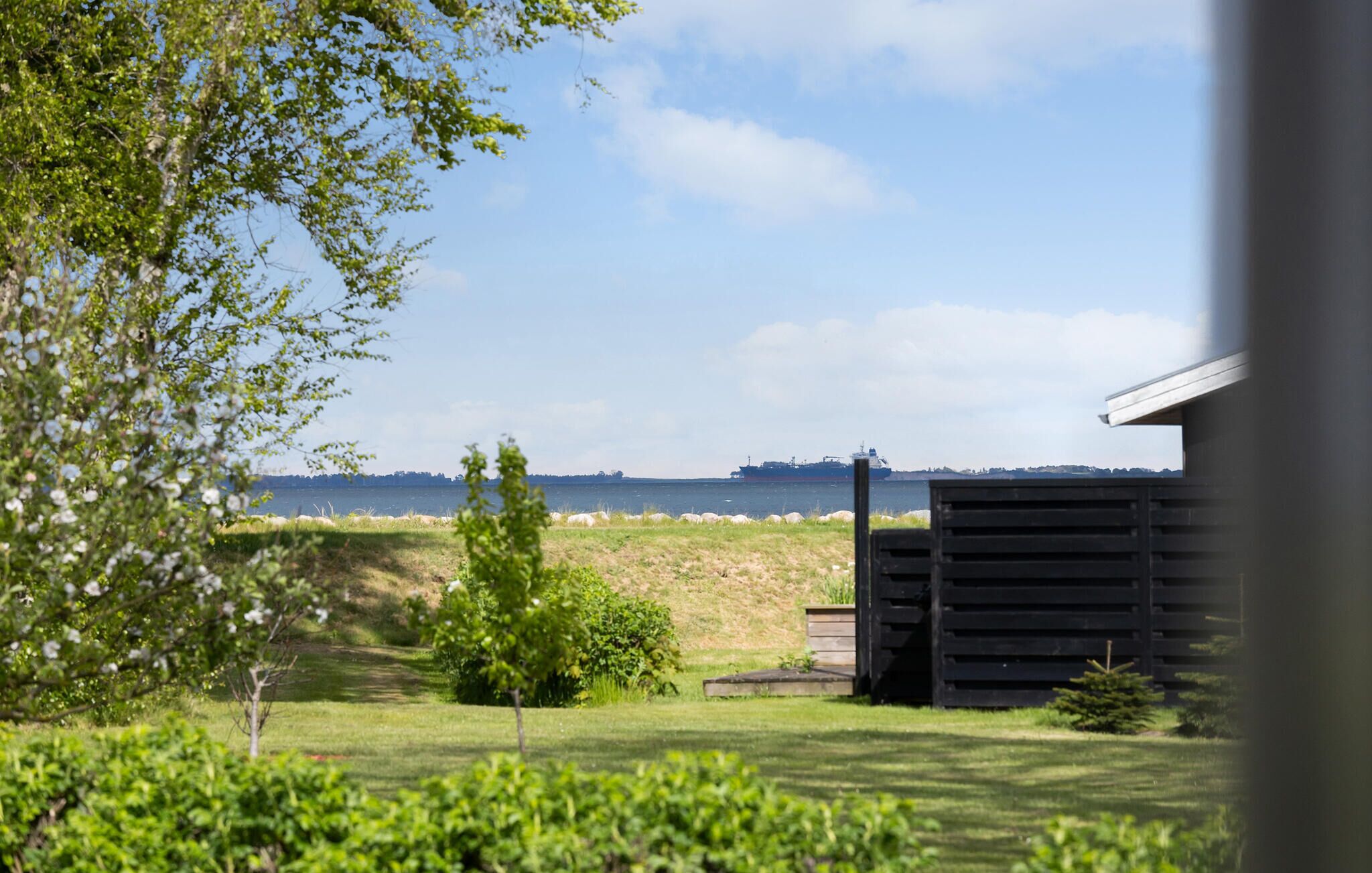 Een grasveld met een klein gebouw, een boom en een schip in de verte op het water.