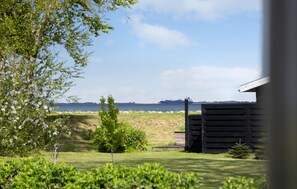 A grassy area with a small building, a tree, and a distant ship on the water. - Cozy home in Otterup with sauna (Otterup)