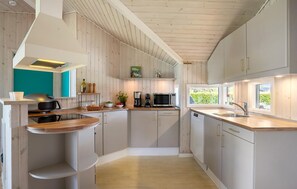 A modern kitchen with wooden cabinetry, a built-in microwave, and a window providing natural light. - Cozy home in Otterup with sauna (Otterup)