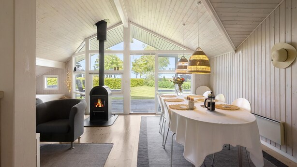 Una habitación acogedora con chimenea, una mesa de comedor lista para cuatro personas y ventanas amplias que ofrecen vistas al exterior.