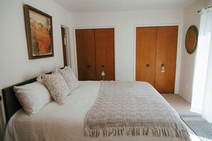 Ein Schlafzimmer mit einem Bett, zwei Holztüren, einem Gemälde und einem Fenster mit Vorhängen.