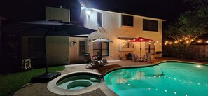 Ein Garten mit Schwimmbad, Terrassenmöbeln und Lichterketten.