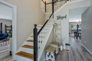 Eine Treppe mit weißen Geländern und Holzstufen, ein Schild mit der Aufschrift 'Blessed' an der Wand und ein Essbereich im Hintergrund.